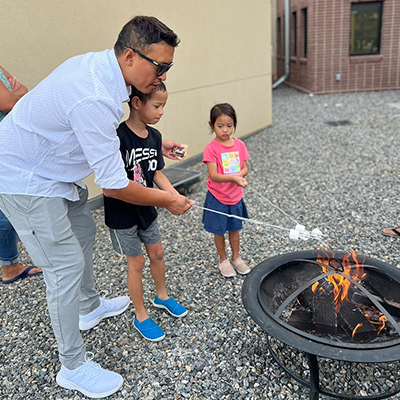 Father and his two children roasting marshmallows over a charcoal grill at a Family Program at the Hudson Public Library