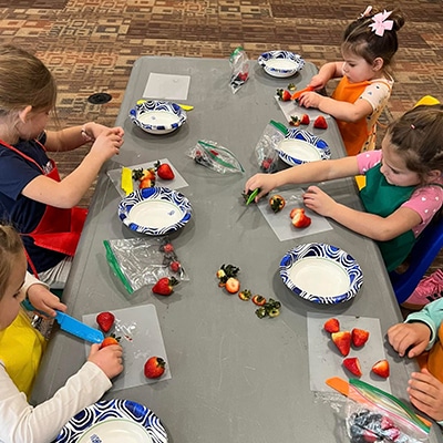 Young children make snacks with fresh fruit during the Tiny Chefs program at the Hudson Public Library